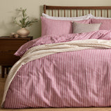 Holme Stripe Cotton Brushed Duvet Cover Set in Rosewood, a pink and white striped duvet with matching pillowcases on a bed with a dark wood headboard, styled with a cream throw in a bedroom setting.