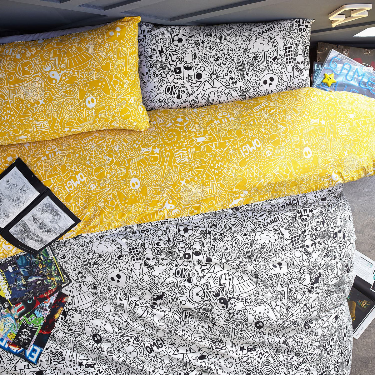 Doodles Polycotton Printed Duvet Cover Set in white/black, reversible to yellow, densely patterned with cartoon doodles, shown on a bed with matching pillowcases.