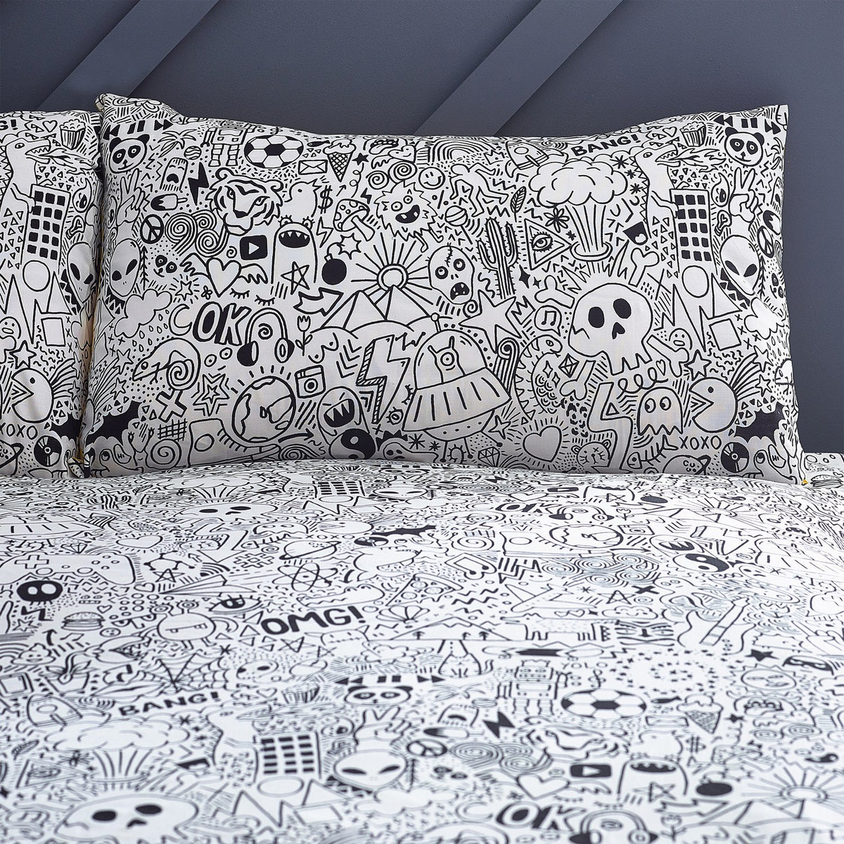 Doodles Polycotton Printed Duvet Cover Set in white/black, pillowcases and duvet covered edge-to-edge with black line-art doodles of aliens, skulls and speech bubbles, shown on a bed.