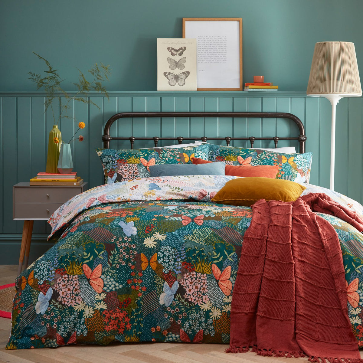 Forage Printed Floral Duvet Cover Set in Teal on a bed with coordinating pillowcases and a rust-red throw, set against teal panelled bedroom walls.