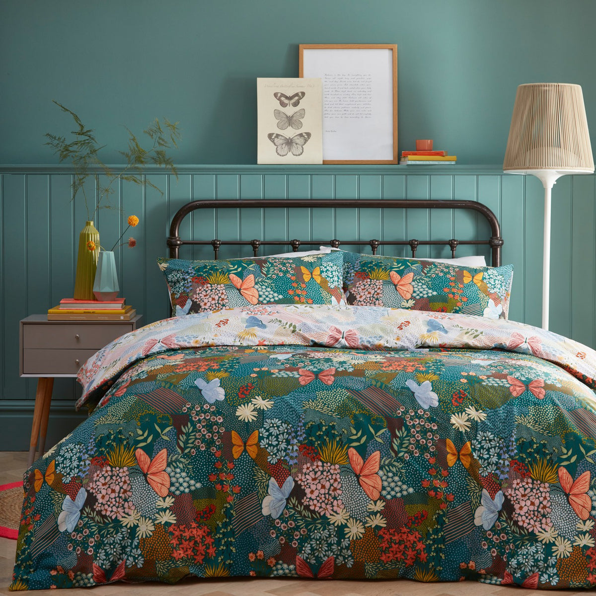 Forage Printed Floral Duvet Cover Set in teal on a bed with matching pillowcases, featuring coral, blue and amber butterflies and floral patchwork print, styled in a teal-panelled bedroom.