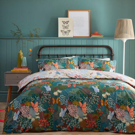 Forage Printed Floral Duvet Cover Set in teal on a bed with matching pillowcases, featuring coral, blue and amber butterflies and floral patchwork print, styled in a teal-panelled bedroom.