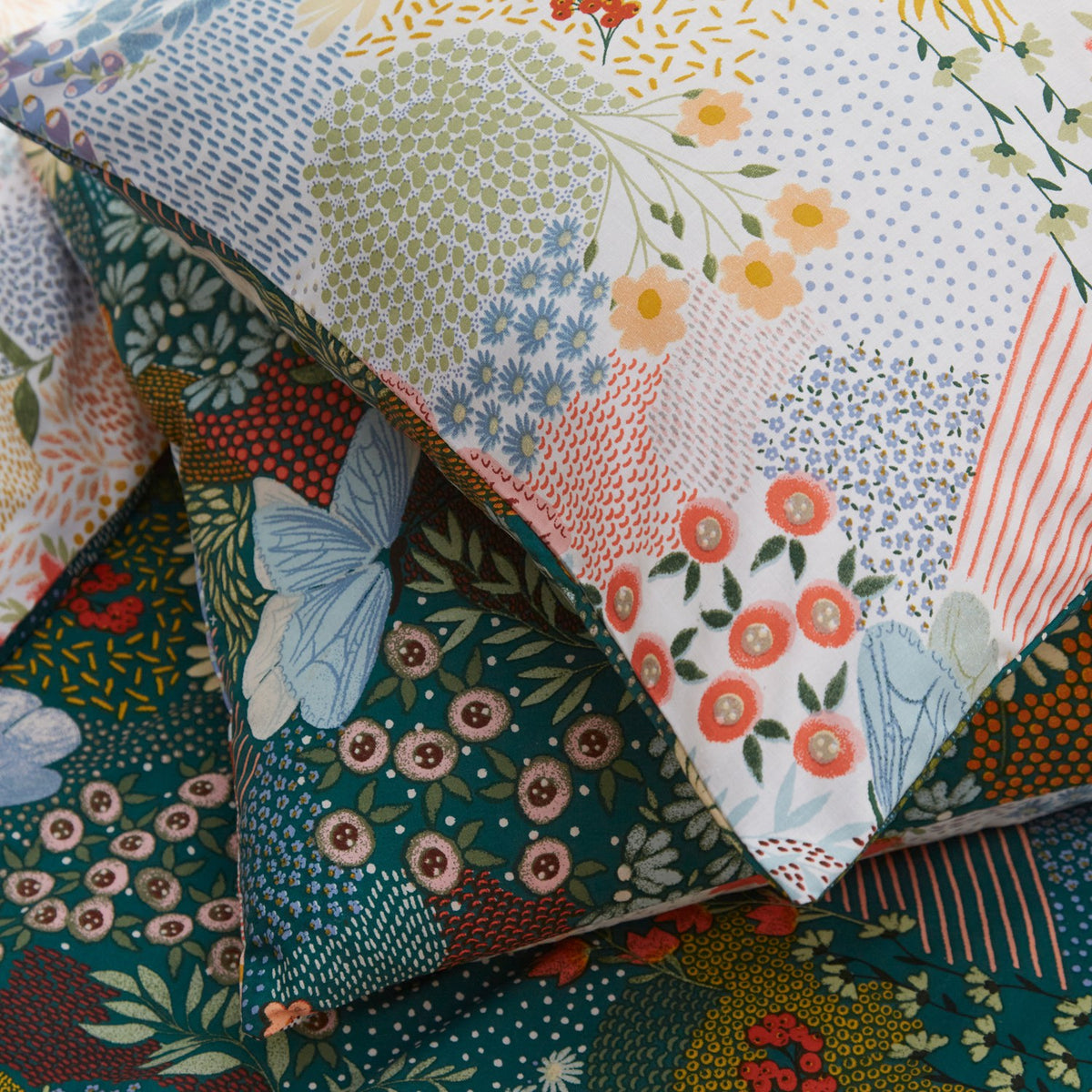 Forage Printed Floral Duvet Cover Set in teal, close-up of pillowcase corner showing patchwork-style floral, butterfly and dot print in coral, blue, amber and green on a deep teal ground.
