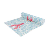 Abersoch Abstract Polyester Table Runner in Marine, partially rolled to reveal a woven blue and white wave pattern with pink lobster and crab motifs, on a plain white background.