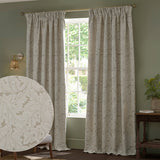 Acanthus Jacquard Linen pencil pleat curtains in beige with ivory-cream leaf pattern, hung at a living room window, with a fabric texture close-up inset.