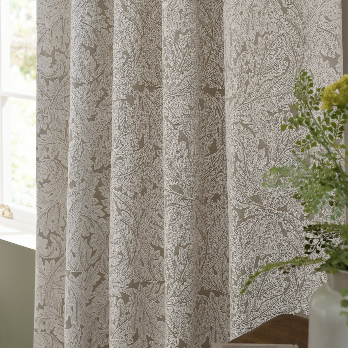 Acanthus Jacquard Linen Pencil Pleat Curtains in beige with ivory-cream woven leaf pattern, shown gathered by a window near a potted plant.