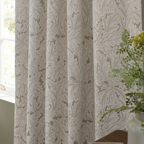 Acanthus Jacquard Linen Pencil Pleat Curtains in beige with ivory-cream woven leaf pattern, shown gathered by a window near a potted plant.
