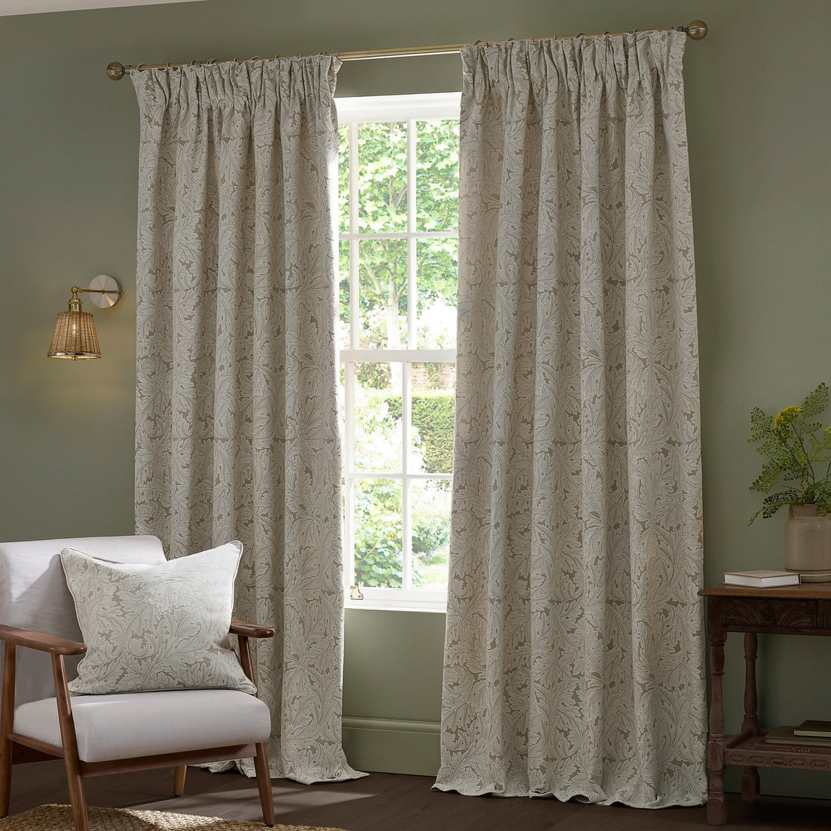 Acanthus Jacquard Linen pencil pleat curtains in beige with an ivory-cream leaf pattern, shown pole-hung either side of a window in a sage-green living room.