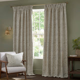 Acanthus Jacquard Linen pencil pleat curtains in beige with an ivory-cream leaf pattern, shown pole-hung either side of a window in a sage-green living room.