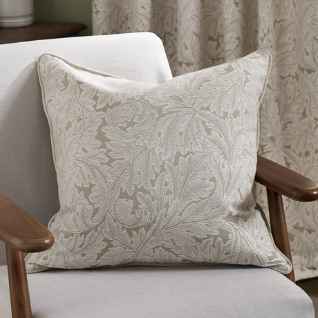 Acanthus Jacquard Linen Cushion in cream, a square cushion with woven acanthus leaf pattern and piped edge, shown on a light upholstered armchair.