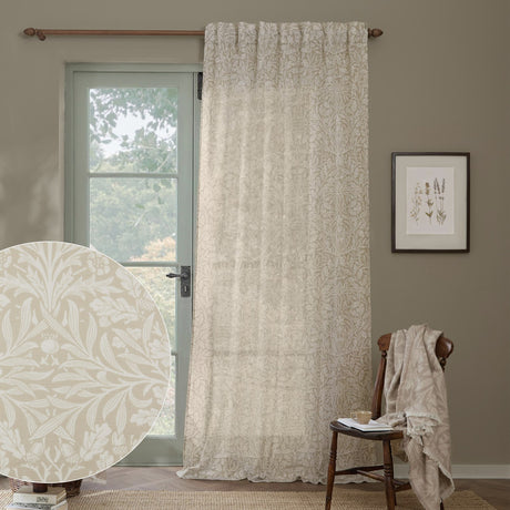 Acorn Damask Linen Curtain Panel in cream, a semi-sheer voile with printed acorn and foliage pattern, shown hung from a wooden rod beside a glazed door in a living room setting.