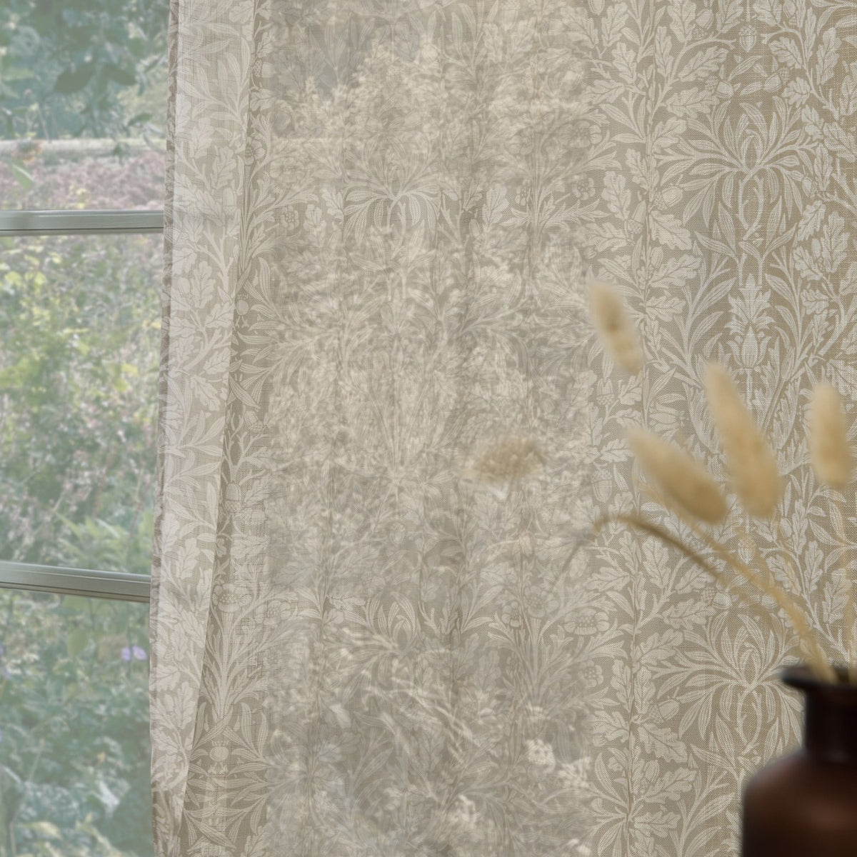 Acorn Damask Linen Curtain Panel in natural cream tones, semi-sheer with a leaf and acorn print, shown hanging at a window beside dried grasses.