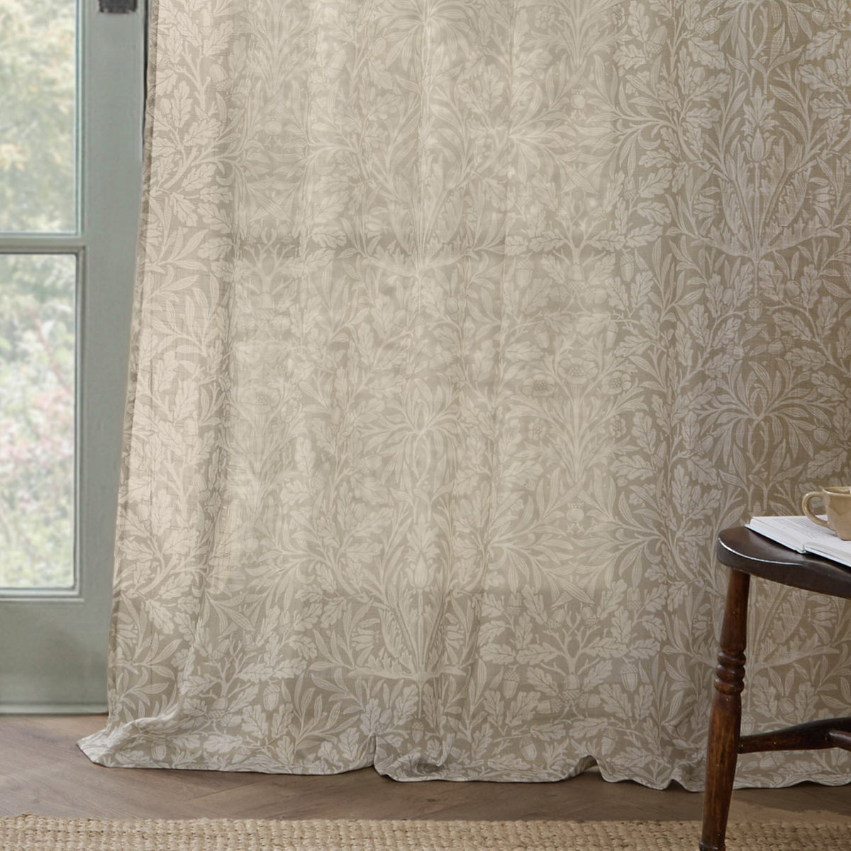 Acorn Damask Linen Curtain Panel in natural cream, semi-sheer voile with printed acorn and foliage design, shown floor-length beside a window in a living room setting.