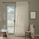 Acorn Damask Linen Curtain Panel in natural cream, hung from a wooden pole beside a glazed door in a living room with a chair, basket, and framed botanical print.