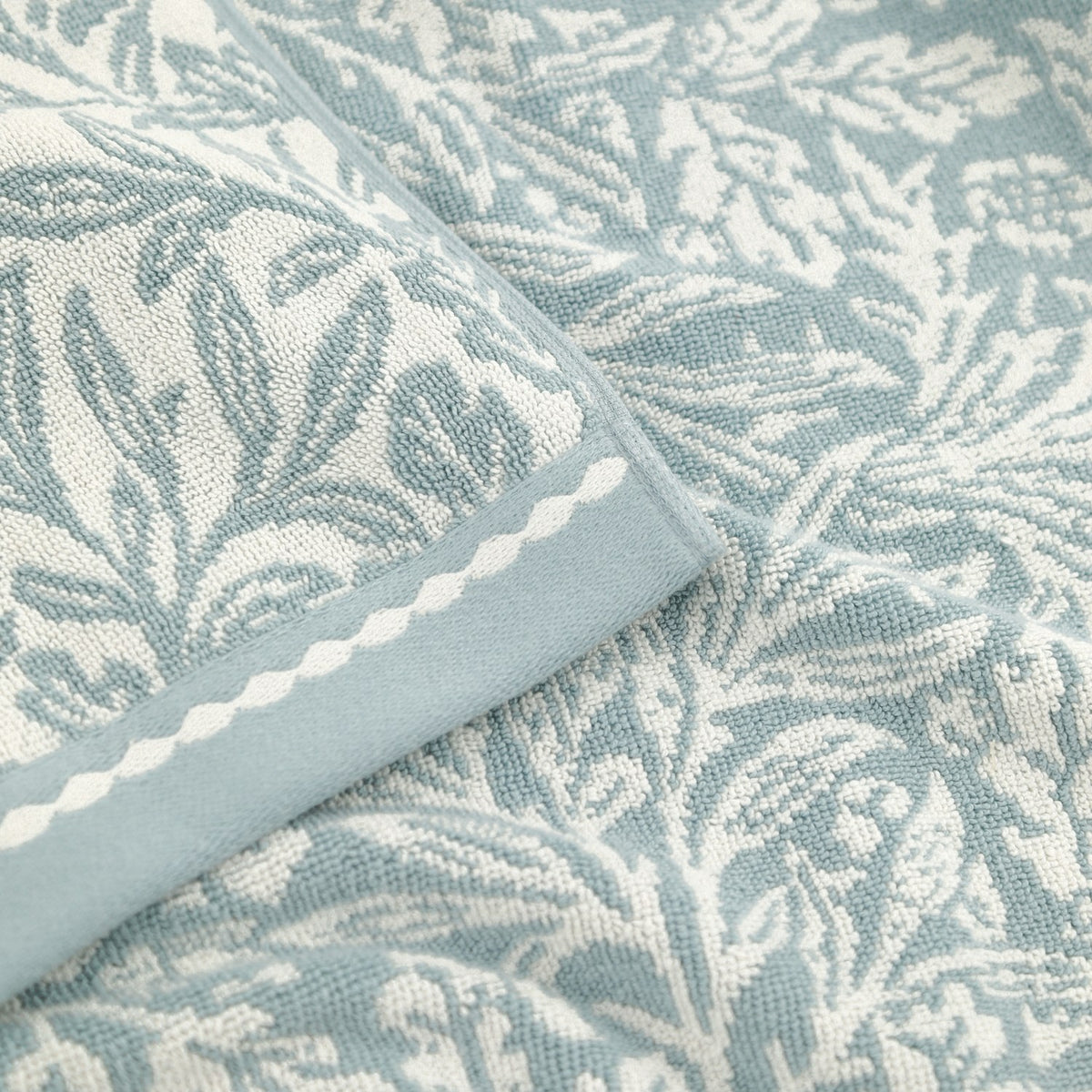 Close-up of Acorn Jacquard Cotton Towels in mineral blue, showing woven acorn and foliage pattern with a scalloped-edge cream border trim.