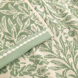 Close-up of Acorn Jacquard Cotton Towel in sage green, showing the woven acorn and foliage pattern with a folded edge trimmed in a contrasting striped border.