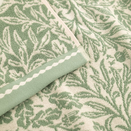 Close-up of Acorn Jacquard Cotton Towel in sage green, showing the woven acorn and foliage pattern with a folded edge trimmed in a contrasting striped border.