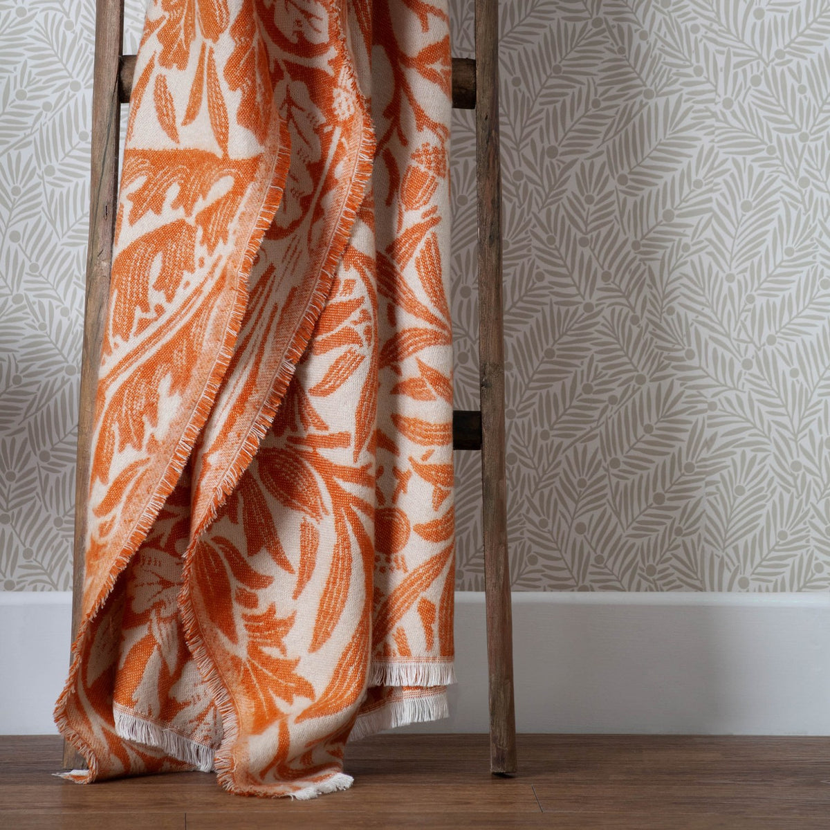 Acorn Tonal Jacquard Cotton Blend Throw in brick orange, draped over a wooden ladder with fringed edges and an all-over oak leaf and acorn pattern on a cream ground.