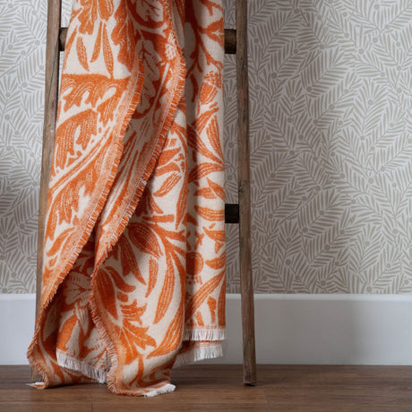 Acorn Tonal Jacquard Cotton Blend Throw in brick orange, draped over a wooden ladder with fringed edges and an all-over oak leaf and acorn pattern on a cream ground.