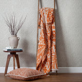 Acorn Tonal Jacquard Cotton Blend Throw in brick orange, draped over a wooden ladder with matching cushion, vase and stool in a living room setting.