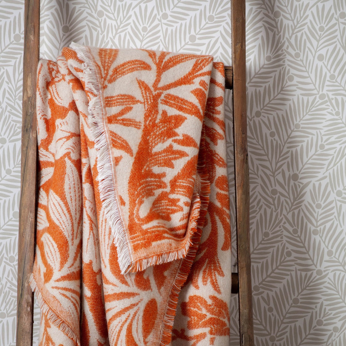 Acorn Tonal Jacquard Cotton Blend Throw in brick orange, draped over a wooden ladder, showing a fringed edge and two-tone leaf and acorn pattern on a cream ground.