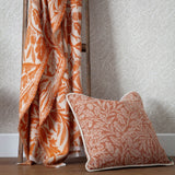 Acorn Tonal Jacquard Cotton Blend Throw in brick orange with fringed edges, draped over a wooden ladder beside a matching cushion and leaf-patterned wallpaper.