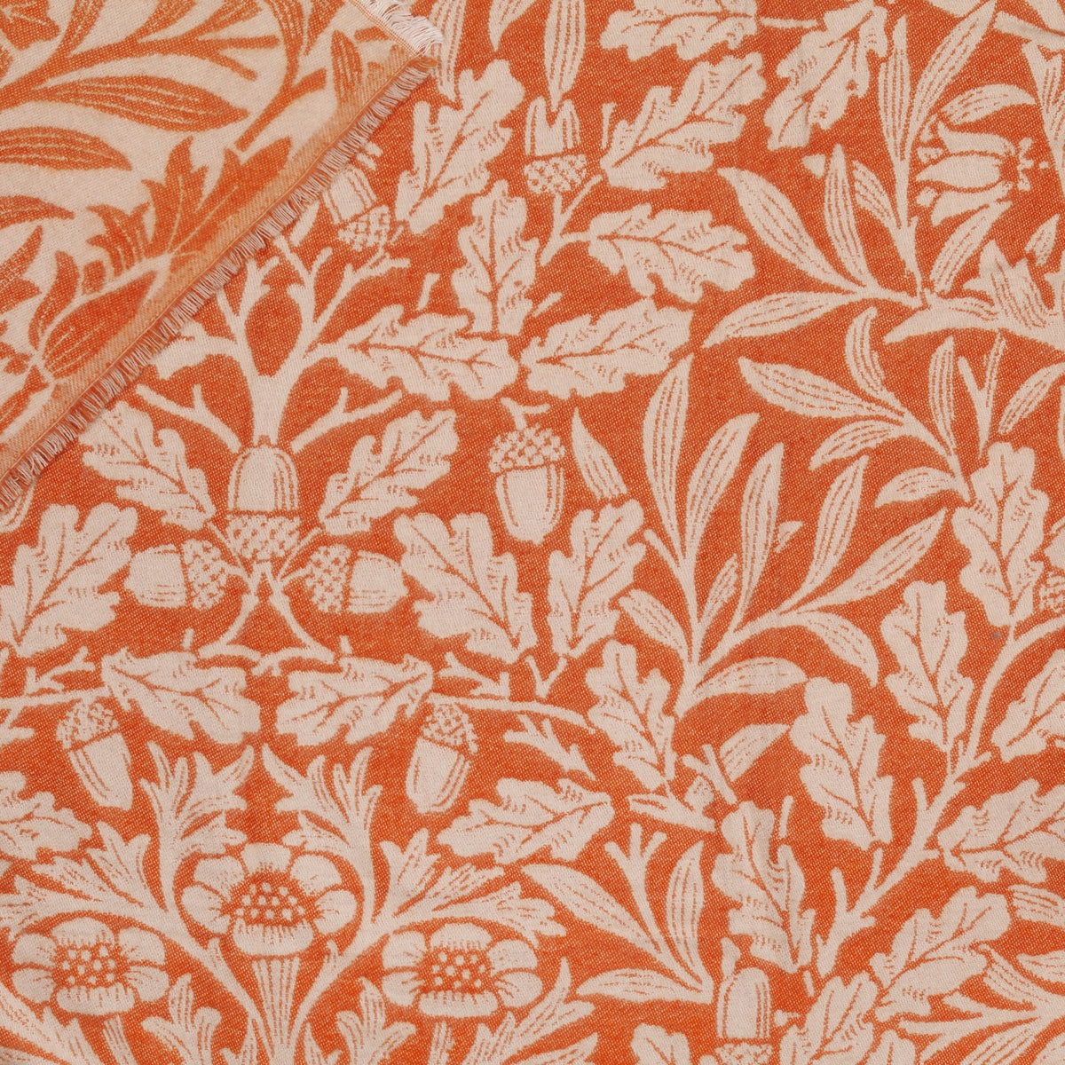 Acorn Tonal Jacquard Cotton Blend Throw in brick orange, woven with a cream oak leaf and acorn botanical pattern, folded corner showing reverse side and fringed edge.