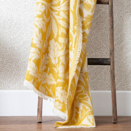 Acorn Tonal Jacquard Cotton Blend Throw in gold and cream, draped over a wooden ladder, showing an oak leaf and acorn pattern with fringed edges.