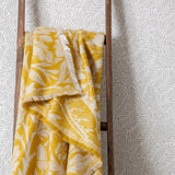 Acorn Tonal Jacquard Cotton Blend Throw in gold and cream, draped over a wooden ladder, showing an oak leaf and acorn pattern with fringed edges.