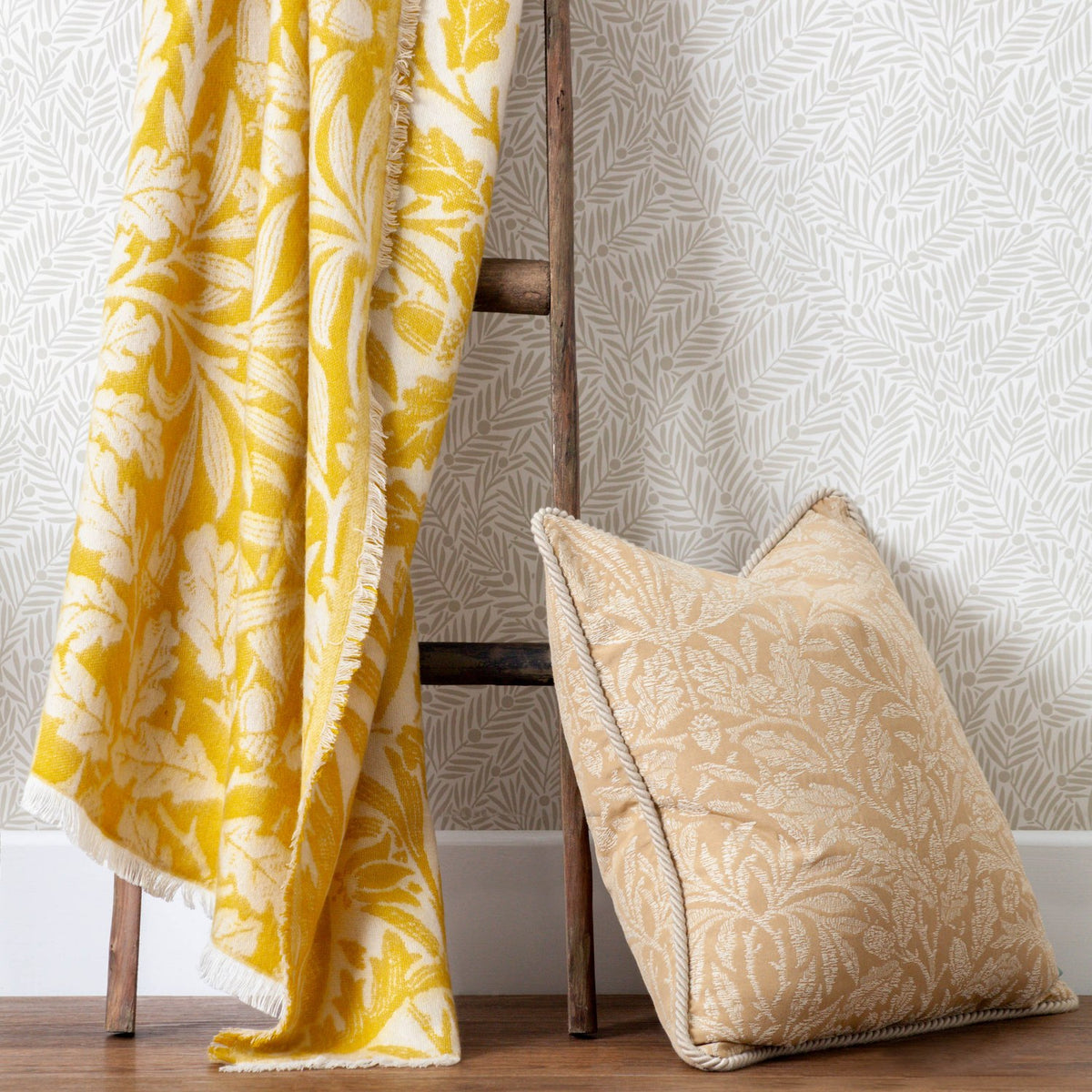 Acorn Tonal Jacquard Cotton Blend Throw in gold and cream, draped over a wooden ladder with a matching gold jacquard cushion, fringed edges visible.