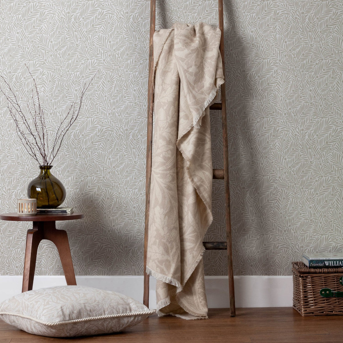 Acorn Tonal Jacquard Linen Throw in beige draped over a wooden ladder, showing its fringed edge and leafy woven pattern in a living room setting.