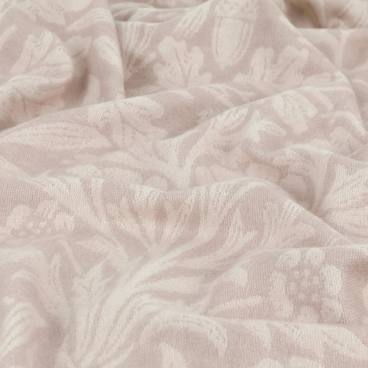 Close-up of the Acorn Tonal Jacquard Linen Throw in beige, showing a woven oak leaf and acorn pattern in soft tonal shades across the draped linen fabric.