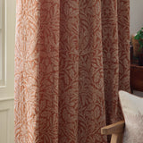 Acorn Tonal Jacquard pencil pleat curtains in brick, showing woven acorn branch pattern in pale cream, hung in pleated folds in a living room setting.