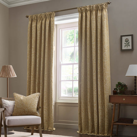 Saffron-gold pencil pleat curtains with tonal Acorn jacquard pattern hang from a bronze pole beside a window in a living room setting.