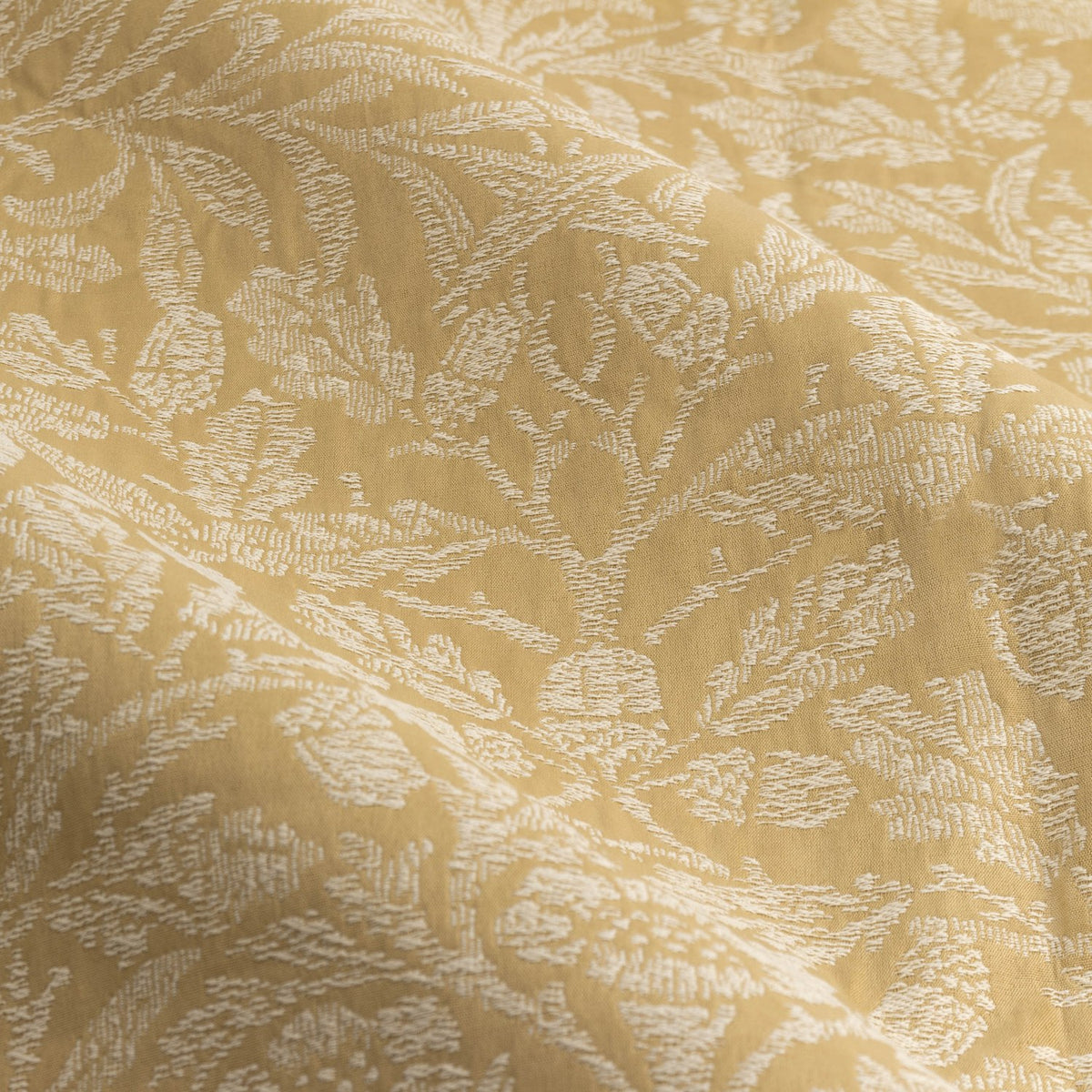 Close-up of Acorn Tonal Jacquard pencil pleat curtain fabric in saffron-gold, showing woven acorn and branch pattern in soft tonal relief across polyester cloth folds.