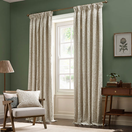 Acorn Tonal Jacquard pencil pleat curtains in Willow, cream leaf-patterned fabric with pencil pleat heading, shown hanging beside a window in a green living room.