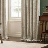 Pencil pleat curtains in Acorn Tonal jacquard, cream fabric with woven acorn and leaf motif, shown pooling at floor beside a window in a living room.
