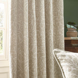 Acorn Tonal Jacquard pencil pleat curtains in Willow, cream fabric with woven acorn and oak leaf pattern, shown hanging in a living room beside a matching cushion.