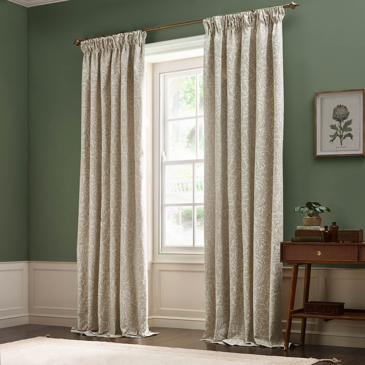 Acorn Tonal Jacquard pencil pleat curtains in cream, hung from a bronze pole beside a bright window in a green-walled living room.
