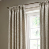 Pencil pleat curtains in linen tone with woven Acorn jacquard leaf pattern, hung either side of a white-framed window with a wooden pole and finials.