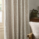 Acorn Tonal Jacquard Linen pencil pleat curtains in beige, woven with an acorn and oak leaf pattern, shown pleated at a window beside a cushion and side table.