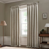Acorn Tonal Jacquard pencil pleat curtains in linen beige with a woven leaf pattern, shown floor-length in a living room beside a window, lamp, and side table.