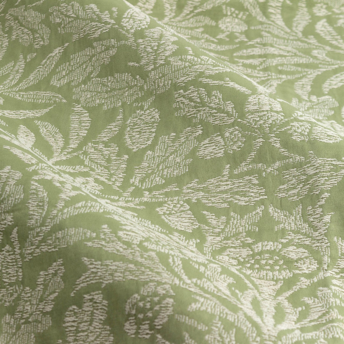 Close-up of Acorn Tonal Jacquard pencil pleat curtain fabric, showing woven oak leaf and acorn motifs in cream against a sage green polyester ground.