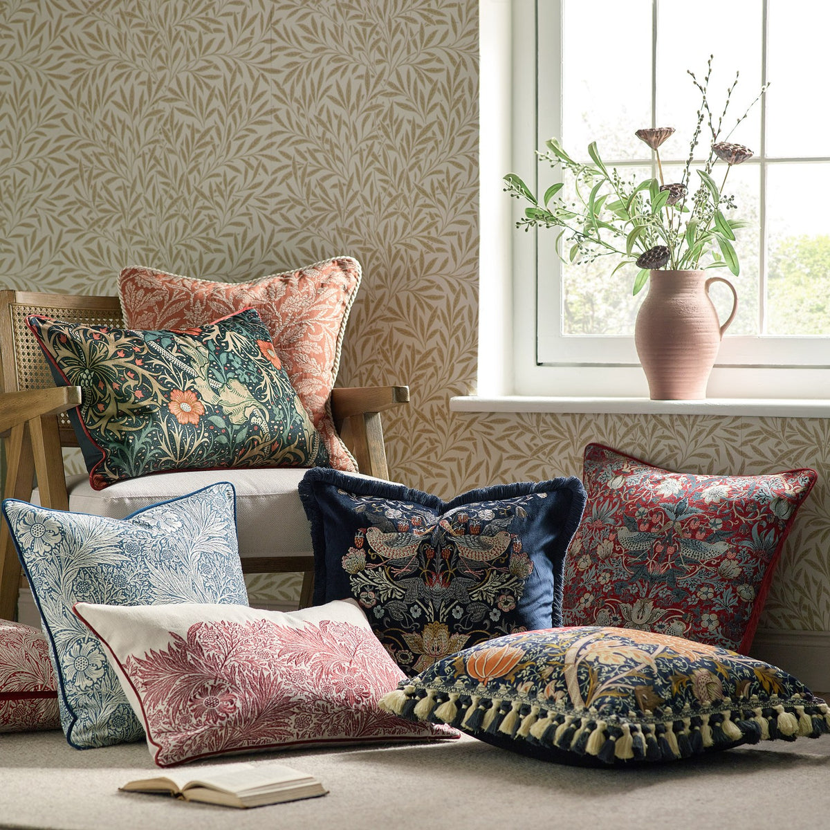 Square patterned cushion in brick-orange jacquard fabric with woven cream acorn and oak leaf motif, shown among William Morris print pillows in a living room setting.
