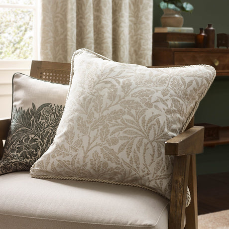Acorn Tonal Jacquard cushion in ivory with woven acorn branch pattern and twisted cord trim, shown on a beige armchair in a living room setting.