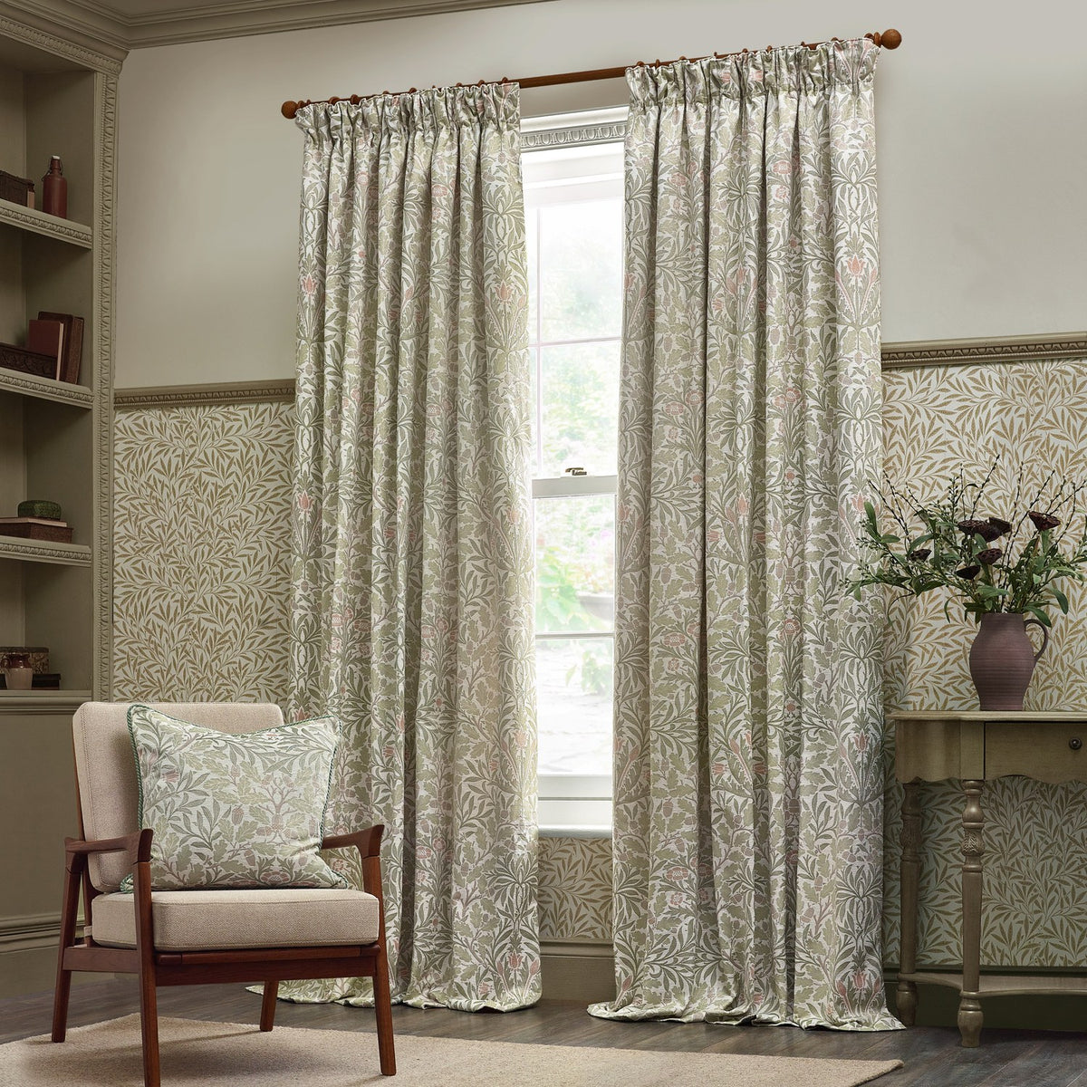 Acorn jacquard chenille pencil pleat curtains in stone and sage, shown pencil-pleated on a wooden pole in a living room with matching cushion, armchair and console table.