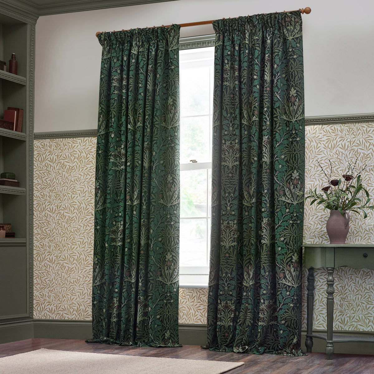 Acorn Multi Chenille Pencil Pleat Curtains in Thyme/Forest, floral acorn and oak leaf jacquard pattern in green tones, hung on a wooden pole beside a window in a panelled study.