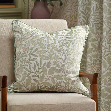 Acorn Multi Jacquard Polyester Cushion in Stone/Sage with woven oak leaf and acorn pattern and cord-trimmed edge, styled on a beige armchair in a living room setting.