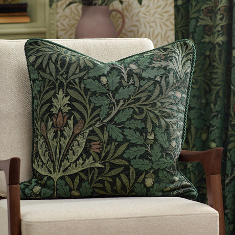 Square jacquard cushion in the Acorn Multi design, woven with oak branches, leaves and acorns in green tones with a corded edge, shown on a cream armchair.