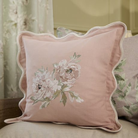 Adele Floral Cotton Cushion in rose pink with scalloped white piping, featuring embroidered floral spray with two blooms and trailing leaves, shown on a sofa.